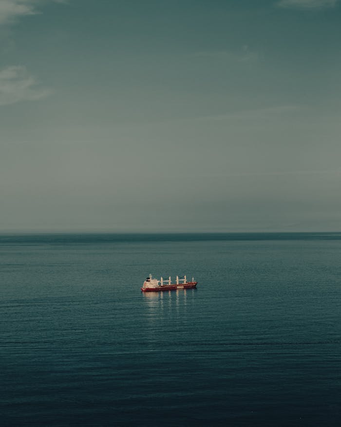 A solitary cargo ship navigates calm blue waters under an expansive sky, capturing serene seascape beauty.
